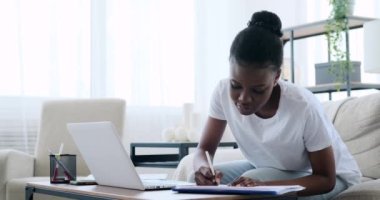 Laptop kullanan ve not yazan Afrikalı Amerikalı bir kadın.