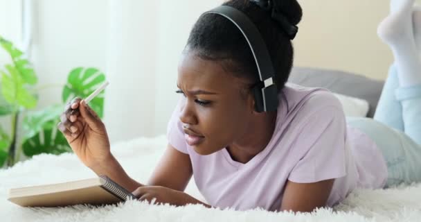 Mujer escribiendo en bloc de notas mientras escucha música en auriculares y canta en la cama — Vídeo de stock