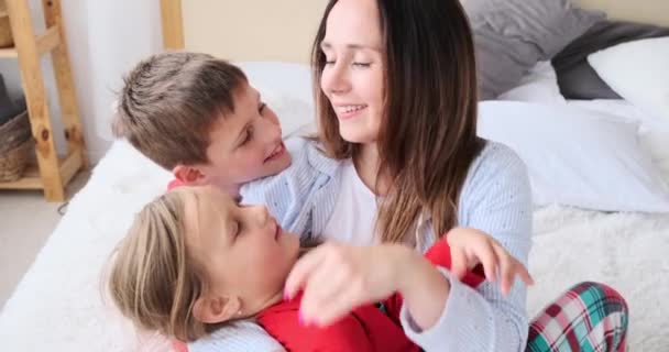 Любящая мать целует своих детей в постели — стоковое видео
