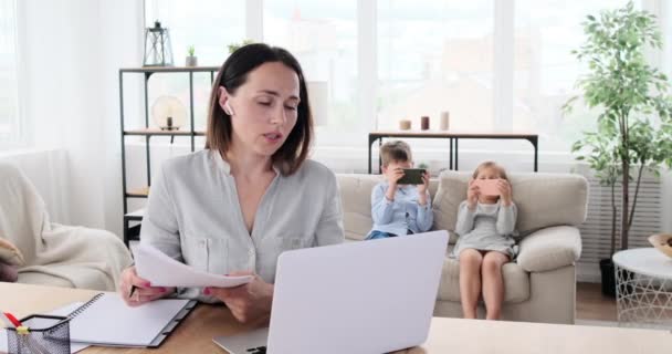 Mor gör videokonferens på bärbar dator med barn som spelar spel på mobiltelefon — Stockvideo