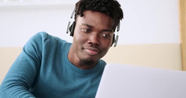 Młody człowiek korzystający z laptopa i słuchający muzyki na słuchawkach w sypialni — Wideo stockowe