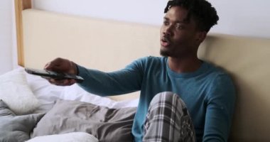 Mutlu genç adam TV izliyor, yatakta dinleniyor.