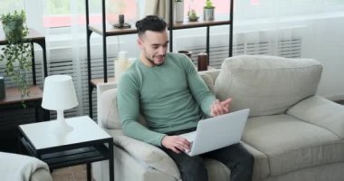 Adam kanepede dizüstü bilgisayar kullanarak görüntülü sohbet ediyor.