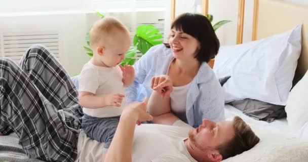 Föräldrar leker med lille son i sängen — Stockvideo