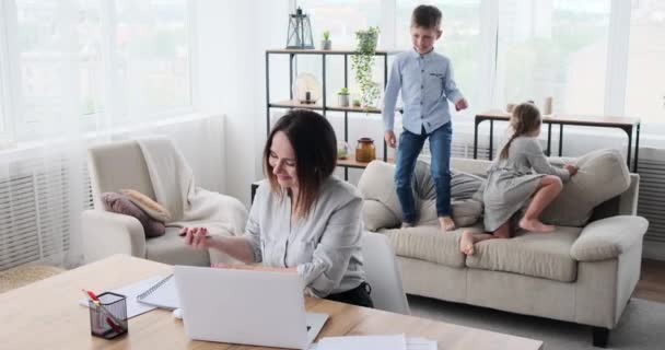 Mãe trabalhando de casa com crianças pulando no sofá — Vídeo de Stock