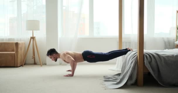 Man doet push-up oefening met opgeheven voeten op bed — Stockvideo