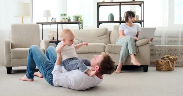Vader spelen met baby zoon terwijl moeder werken op laptop — Stockvideo