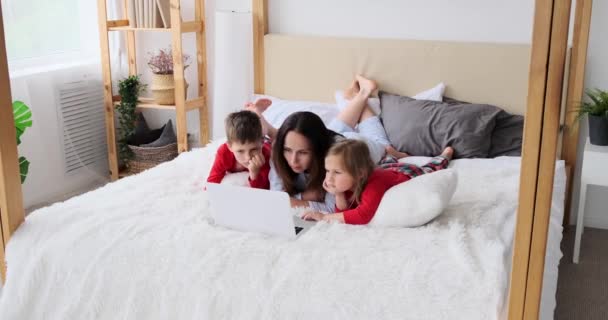 Мати з дітьми дивиться фільм за допомогою ноутбука на ліжку — стокове відео