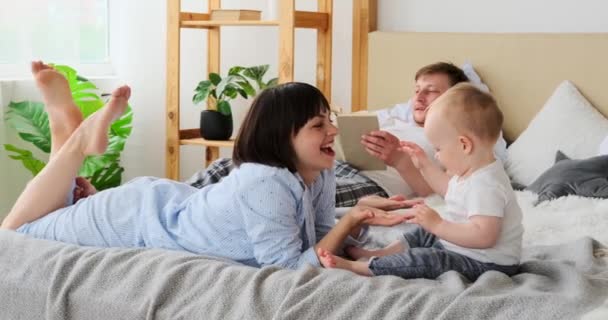 母親遊びともに赤ちゃん息子一方父読書本上のベッド — ストック動画