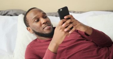 Adam yatakta dinleniyor ve cep telefonu kullanıyor.