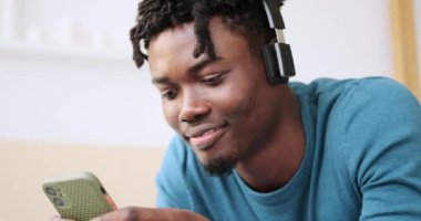 Genç adam cep telefonu kullanıyor ve kulaklıkla müzik dinliyor.