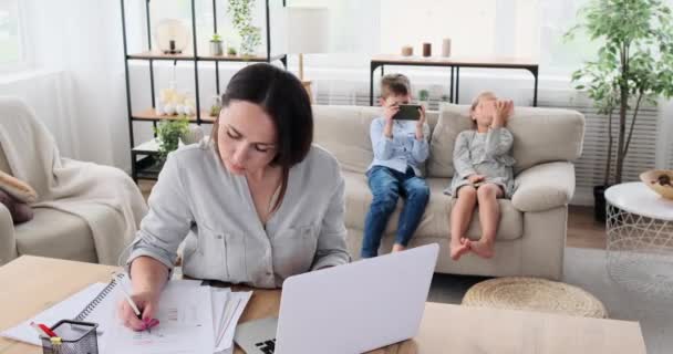 Moeder werken met behulp van laptop, terwijl kinderen het spelen van spel op mobiele telefoon — Stockvideo