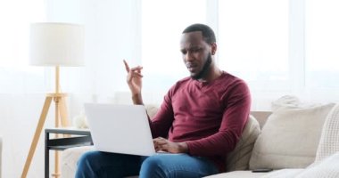 Kanepede dizüstü bilgisayar kullanan kafası karışmış bir adam.