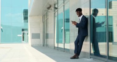 İş adamı kahve içiyor ve ofis binasının dışında cep telefonu kullanıyor.