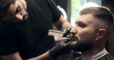 Berber, bıyığı makasla kesiyor.