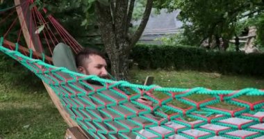 Genç adam hamakta yatarken cep telefonu kullanıyor.