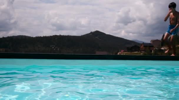 Garçon éclaboussant l'eau tout en sautant dans la piscine — Video