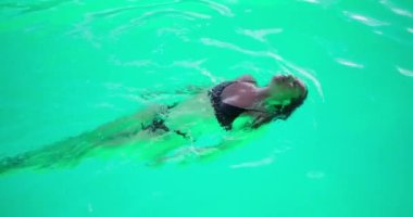 Havuzda sırt üstü yüzen genç bir kadın