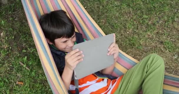 Junge benutzt digitales Tablet während er auf Hängematte liegt — Stockvideo