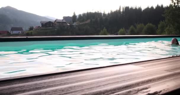 Mujer joven nadando en la piscina contra el paisaje escénico — Vídeos de Stock
