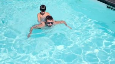 Oğlu sırtında havuzda yüzen gömleksiz bir baba.