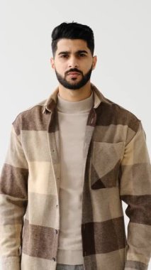 Genç yetişkin bir adam beyaz bir arkaplanda duruyor, ciddi bir ifadeyle kameraya bakıyor ve elleriyle bir dur hareketi yapıyor..