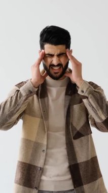 Genç bir yetişkin adam beyaz bir zemine dayanır, şiddetli baş ağrısı, migren ya da acı içinde başını tutarken hastalık belirtileri gösterir..