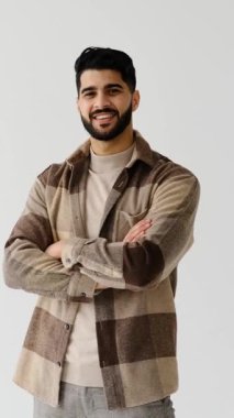 Sakallı, yakışıklı ve şık bir yetişkinin portresi beyaz bir arka planda duruyor, gülümsüyor ve kameraya güvenle poz veriyor..