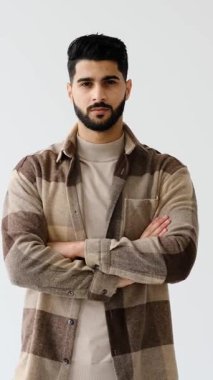 Yakışıklı ve şık sakallı genç bir adamın portresi, kollarını beyaz bir arka plana kavuşturmuş ve kendinden emin bir ifadeyle kameraya bakıyor..