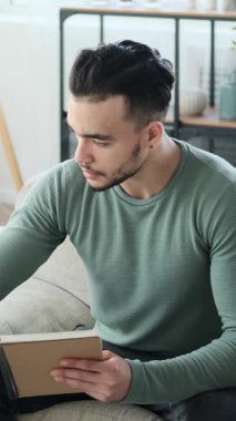 Düşünceli bir genç adam evdeki bir koltukta oturur ve düşüncelerini, planlarını ya da notlarını bir deftere yazar..