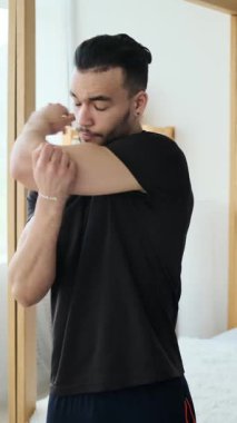 Spor kıyafetleri içinde genç bir adam egzersiz rutinine başlamadan önce kollarını, omuzlarını ve boynunu uzatarak ısınıyor..