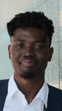 Yakışıklı ve kendine güvenen, takım elbiseli siyahi bir iş adamının açık havada kameraya içten bir şekilde gülümseyen yakın çekim portresi..