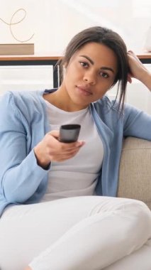 Genç yetişkin bir siyahi kadın, TV 'de izleyecek ilginç bir şey bulunca sıkılmış ve mutlu olmuş ifadesini değiştiriyor ve bunu kutluyor..