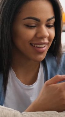 Genç bir siyahi kadının evdeki kanepede dinlenirken gülümsemesi sosyal medyada gezinmesi ya da akıllı telefonunda mesajlaşması..