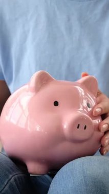 Bir kadının ABD doları banknotunu katlayıp pembe bir kumbara içine koyması. Tasarruf, kişisel finans ve ekonomi kavramı.