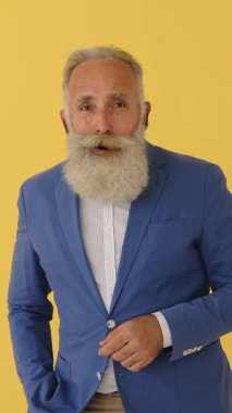 Şaşırmış, beyaz sakallı, şokla tepki veren, inançsızlıkla gözlerini ovuşturan, sonra da gülümseyen kıdemli bir adam. Sarı stüdyo geçmişi. Dikey video.