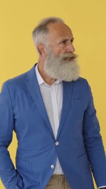 Uzun sakallı sabırsız bir kıdemli adam saatini kontrol eder, bekler, sinirli bakar ve gider. Sarı stüdyo geçmişi. Dikey video.