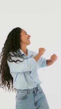 Kıvırcık saçlı, dans eden ve etrafında dönen enerjik genç bir kadın. Mutlu kadın model eğleniyor, özgürce hareket ediyor ve beyaz arka planda izole edilmiş müzikten zevk alıyor..