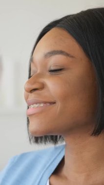 Kapalı gözlerle gülümseyen diş telleri olan mutlu bir Afrikalı Amerikalı kadının yakın plan profili. Neşeli ve rüya görüyor. Evinde tek başına..