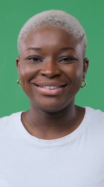 Kısa boyalı saçlı, gülümseyen ve gülen mutlu bir Afrikalı Amerikalı kadının yakın plan portresi. Yeşil arka planda izole edilmiş kameraya bakıyor..