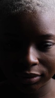 Kısa saçlı, dramatik ışıklandırmalı ve kameraya bakan Afro-Amerikan bir kadının yakın portresi. Dikey video siyah arkaplanda izole edildi.