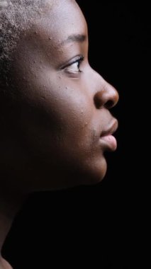 Dramatik bir şekilde gülümseyen Afro-Amerikan bir kadının profil portresi. Dikey video siyah arkaplanda izole edildi.