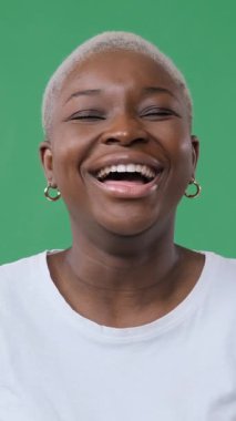 Neşeli, Afro-Amerikan bir kadının sesli kahkahalarla güldüğü portreyi yakından çek. Yeşil arkaplanda dikey video izole edildi.