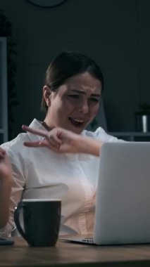 Sandalyede dans eden ve gece geç saatlerde dizüstü bilgisayarda başarıyı kutlayan heyecanlı genç iş kadını. Kahve içen mutlu bayan çalışan. Dikey video.