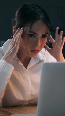 Stresli genç iş kadını gece geç saatlere kadar çalışıyor, notları kontrol ediyor ve endişeli telefon görüşmeleri yapıyor. Çok çalışan kadın çalışanın başı ağrıyor. Dikey video.