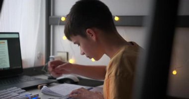 Evde ders çalışan, dizüstü bilgisayar kullanan, uzaktan öğrenme sırasında cetvel ve kalemle çizim yapan bir çocuk..