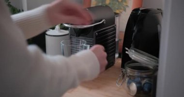 Kadın ellerinin kahve makinesine kapsül sokup düğmeye basmasını kapatın. Kadın evde mutfakta taze espresso yapıyor. Sabah rutini.