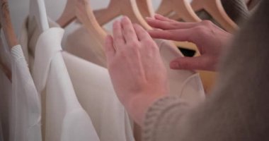 Askıdaki kazak ve gömlekleri sıralayan kadın ellerini kapat. Elbise dolabından kıyafet seçen bir kadın..