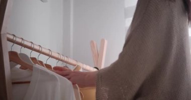 Yatak odasından elbise seçen bir kadının dikiz manzarası. Askıları süveterlerle ayıran ve sarı olanı seçen kadın elleri. Evde rutin hazırlıklar yapılıyor..