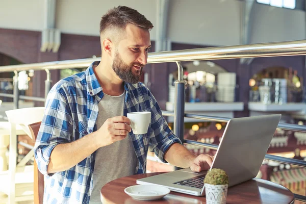 Mann trinkt Kaffee und benutzt Laptop in Café — Stockfoto